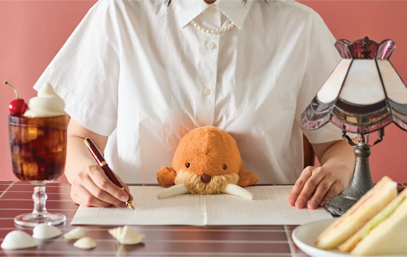 Posture Pal - Marine Walrus accompanies writing, surrounded by a sundae, sandwiches, and stones on a cozy desk, perfect for comfort and motivation.