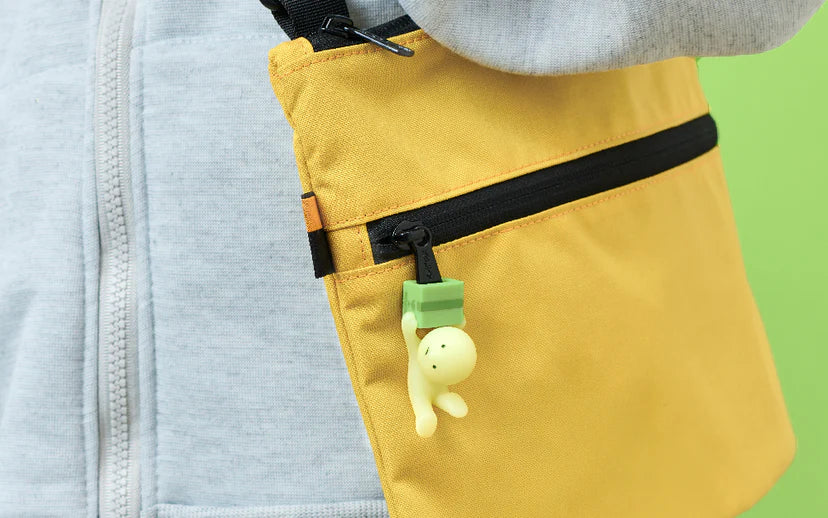 SMISKI ZIPPERBITE - Vol. 2: A yellow shoulder bag with a black zippered pocket, featuring a glowing SMISKI charm hanging from the zipper, adding playful charm.