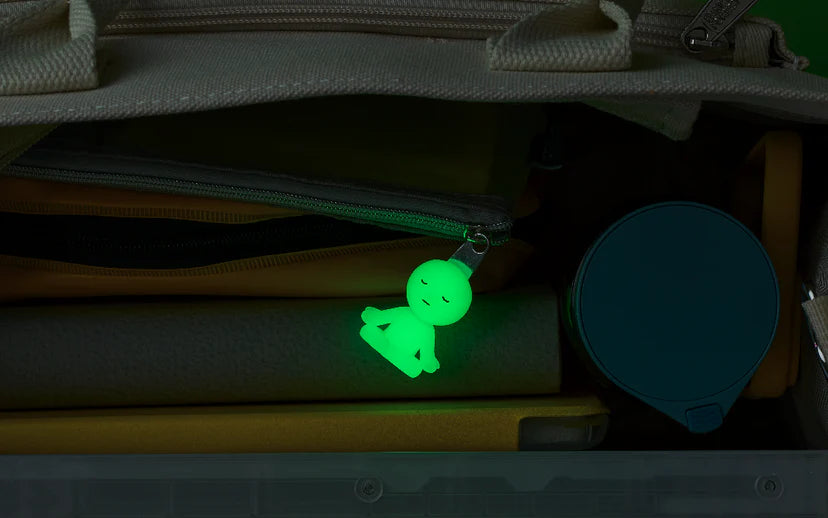 SMISKI ZIPPERBITE - Vol. 2 keychain glows inside a bag, clipped to a zipper, alongside folders and a drink container, perfect for everyday carry.
