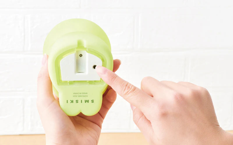 A person points at a green Smiski Touch Light, featuring Smiski and Smiskitty. Tap to adjust brightness levels. Micro USB charger included. Dimensions: W83 x D92 x H173mm.