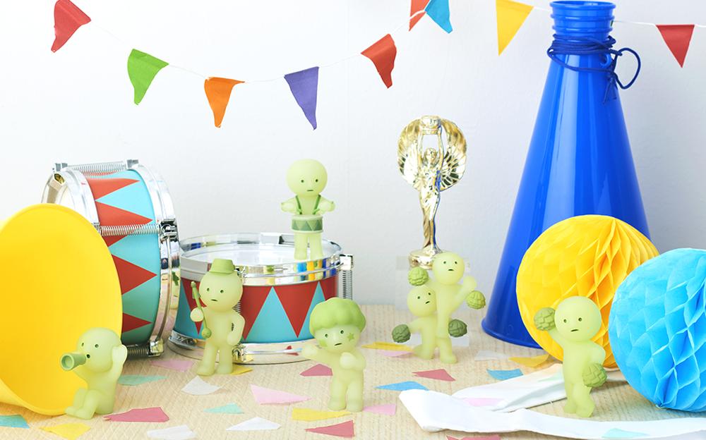 SMISKI Cheer series: Small figurines, toy bear with drum, balloon bear, cone, paper ball, and gold statue on table.