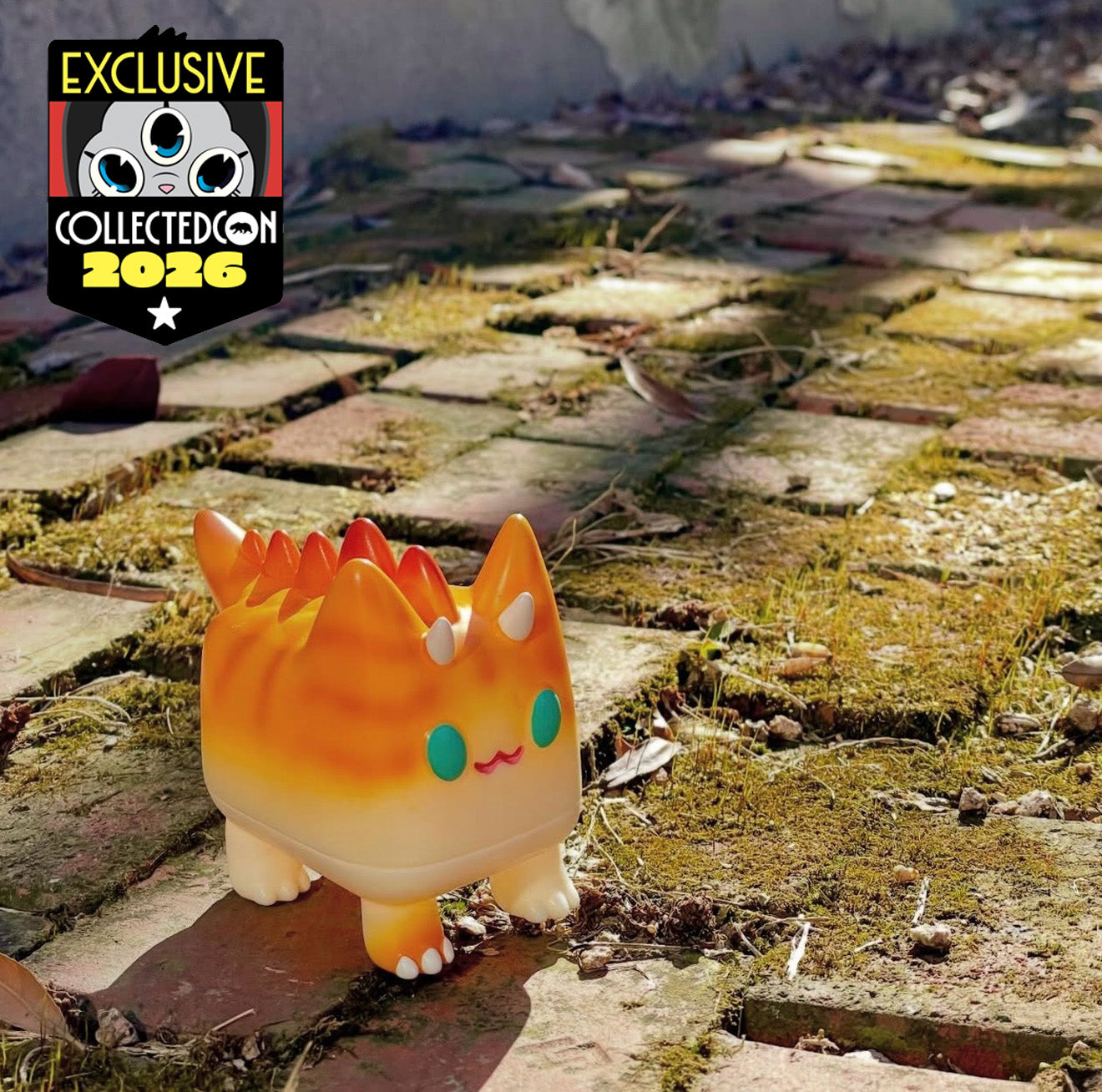Orange Dino Kitty by Rato Kim, a small, horned cat-like figure in a soft gradient finish, exclusive to Collected Con 2026, on a mossy path.