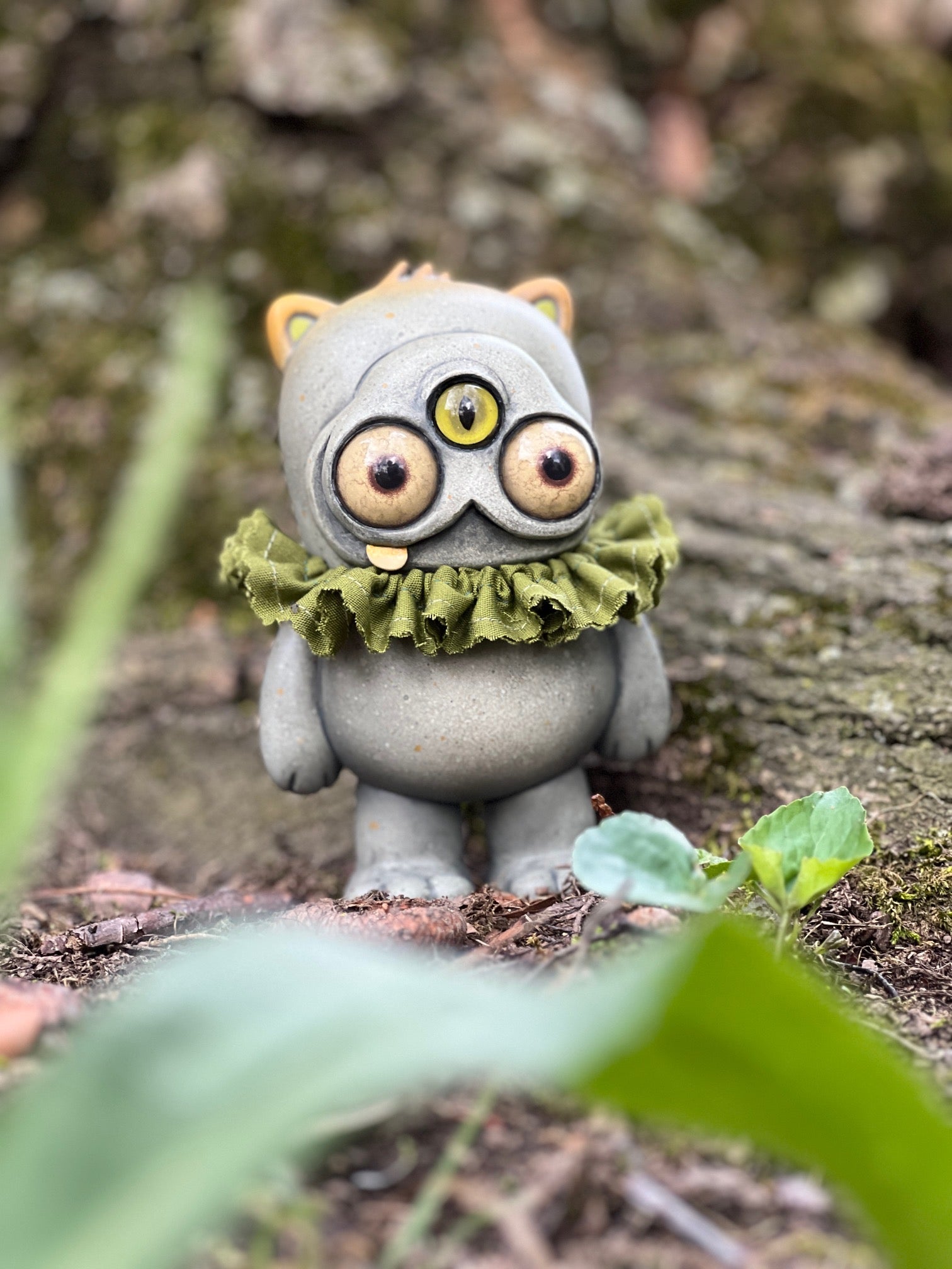 Beans Group Show - Ruffletoof Beans figurine, 5 vinyl, with three eyes and green ruff, sitting on a forest floor. Preorder for May 2026.