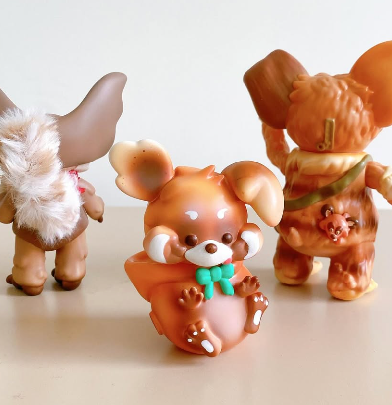 Thief Raccoons by Vivian Wang: Three stylized vinyl figures, including a chubby creature with big ears and two anthropomorphic animals, embodying a warm brown palette.