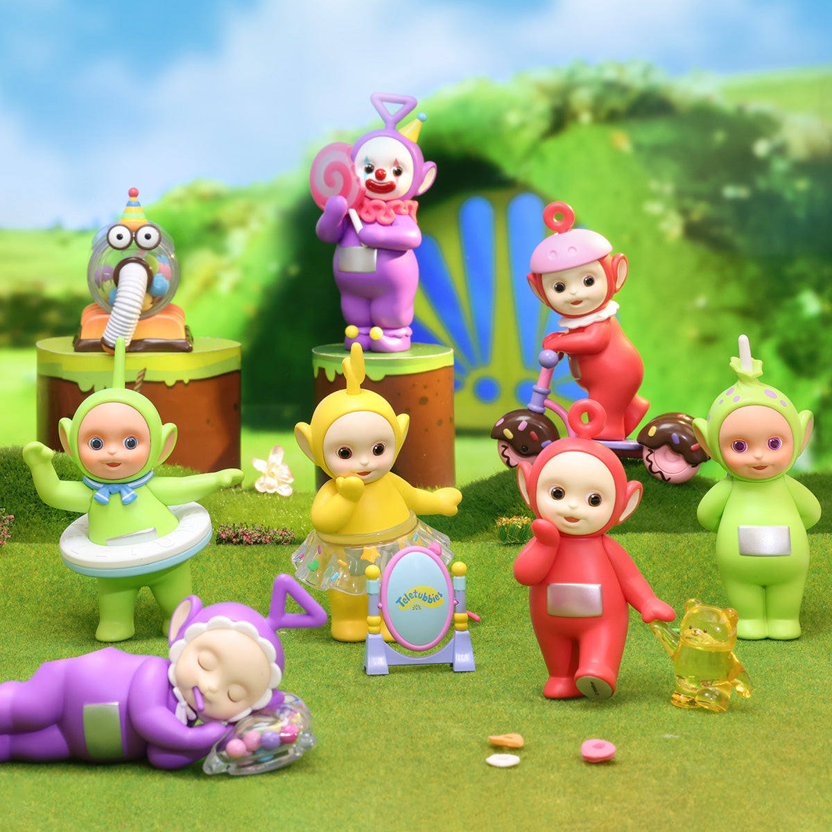 Teletubbies Fantasy Candy World Series - Preorder: Playful scene with colorful Teletubby figurines in whimsical outfits, set in a grassy playland with candy accents.