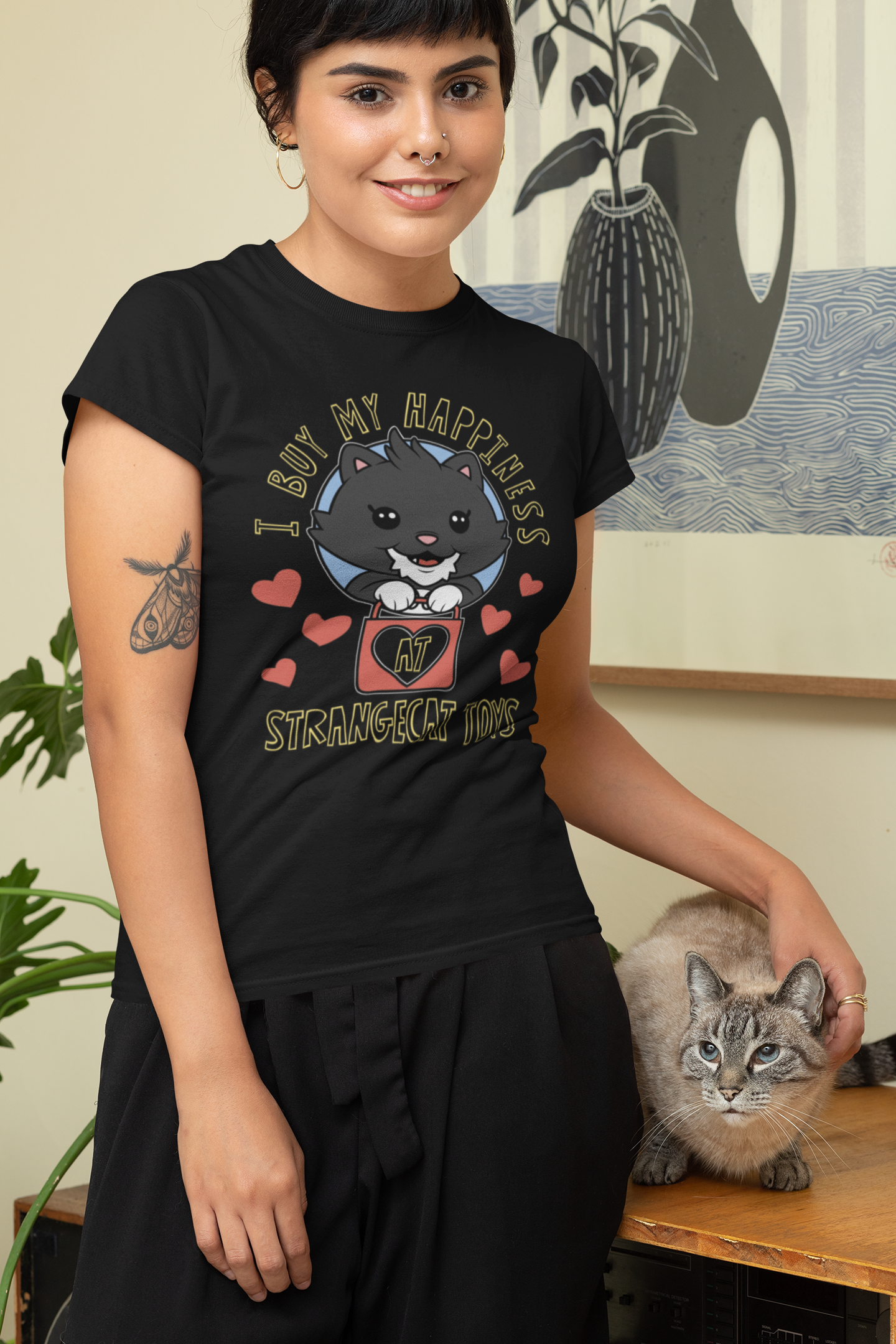 Woman in a black I Buy My Happiness t-shirt with a cartoon cat design, smiling and petting a cat.