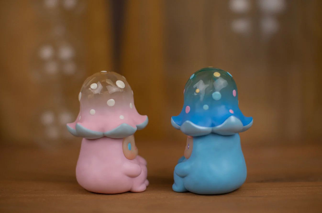 Two stylized vinyl figurines, including the Blue Loliboom mushroom by Pucky, featuring polka-dotted caps and rounded bodies, viewed from behind.
