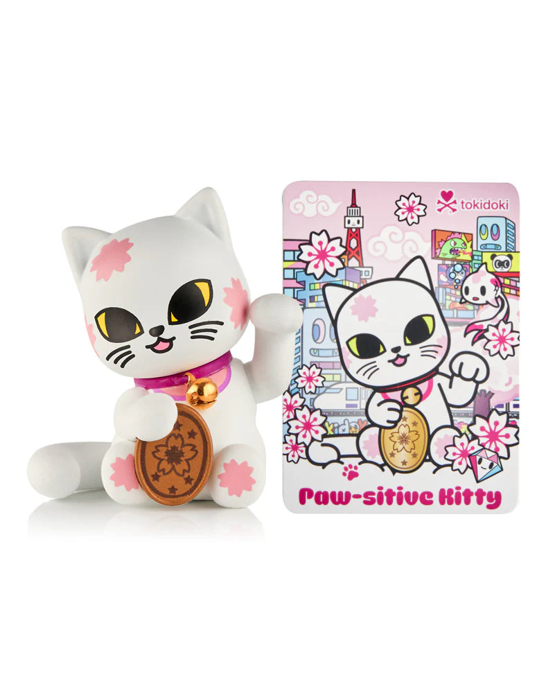 tokidoki's Lucky Cats Blind Box: White vinyl Maneki-neko with cherry-blossom decals, gold coin, and character card in Tokyo backdrop, featuring Paw-sitive Kitty.