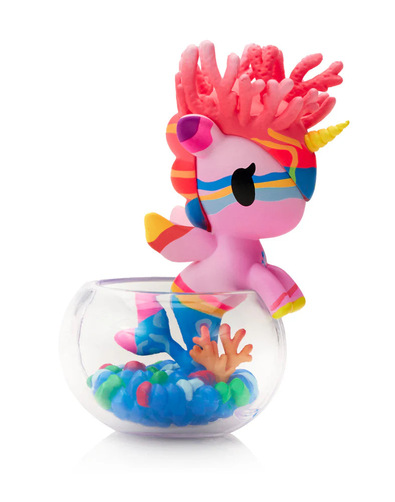 Neon Reef Mermicorno Blind Box figurine atop a fishbowl, featuring pink unicorn with rainbow accents and coral mane amidst colorful gravel and coral decoration.