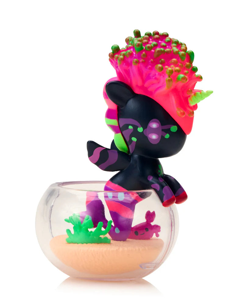 Neon Reef Mermicorno Blind Box: Black mermaid unicorn figure with neon-pink coral hair in a mini aquarium with sandy base and seaweed, collectible art toy.
