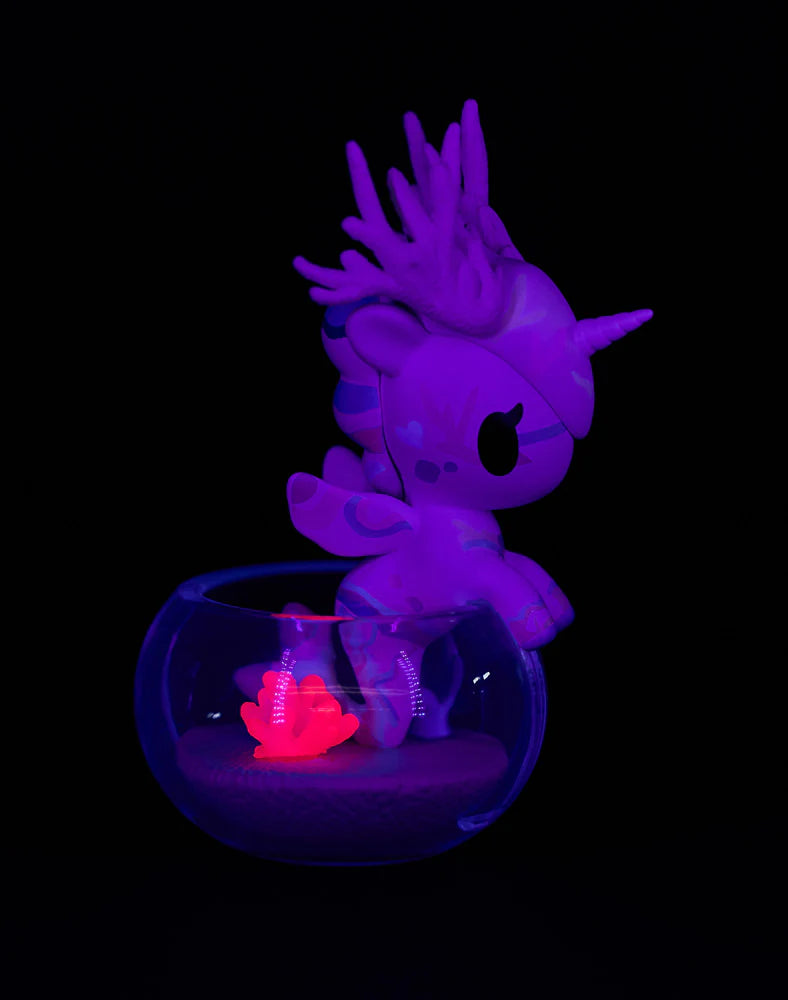 Neon Reef Mermicorno Blind Box figurine perched on a sand-filled glass bowl, illuminated under UV light, showcasing its glowing coral-themed design.