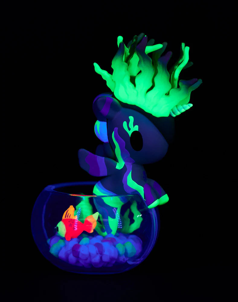 Neon Reef Mermicorno Blind Box showing a purple unicorn figure with glowing green mane on a fishbowl rim, featuring fluorescent fish and pebbles inside.