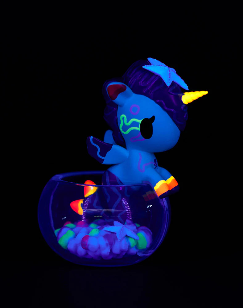 Neon Reef Mermicorno Blind Box figurine with wings and neon markings, perched on a glass bowl with glowing pebbles under blacklight.
