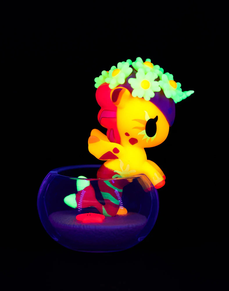 Neon Reef Mermicorno figure on glass bowl, glowing under blacklight. Part deer, part pony, with neon colors and daisy crown. From Strangecat Toys' blind box collection.