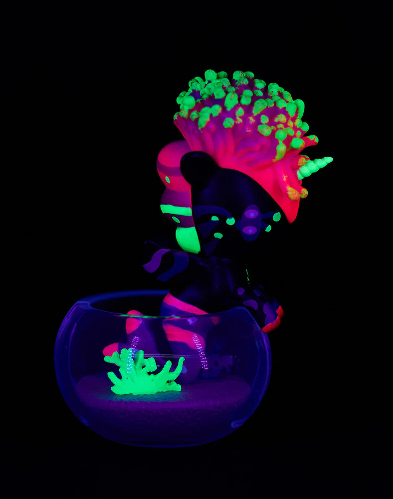 Neon Reef Mermicorno Blind Box featuring a glowing unicorn-zebra hybrid figurine in a glass bowl with neon coral, illuminated under blacklight.