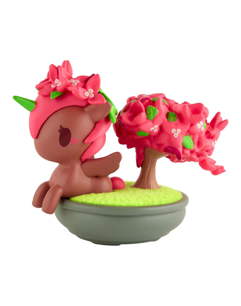Botanical Bonsai Unicorno Blind Box figurine: chibi unicorn with brown body, pink mane, green horn, lounging by cherry-blossom tree in a gray pot.