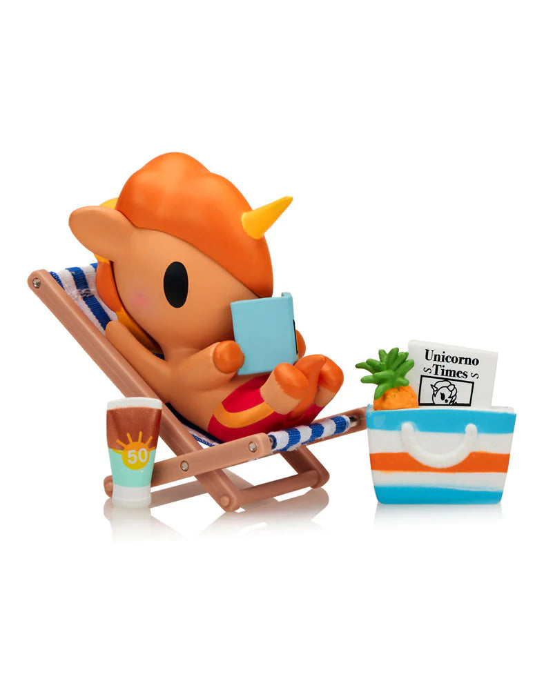 Fun In The Sun Unicorno Blind Box: A vinyl unicorn figurine relaxes on a striped beach chair, reading, with a sunscreen bottle and striped tote beside it.