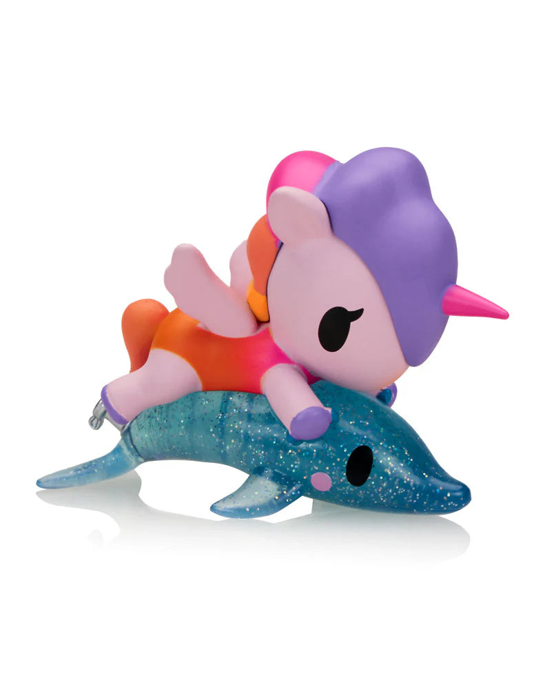 Fun In The Sun Unicorno Blind Box toy features a pink-winged unicorn on a glittery dolphin, highlighting collectible charm for beach-themed fun.
