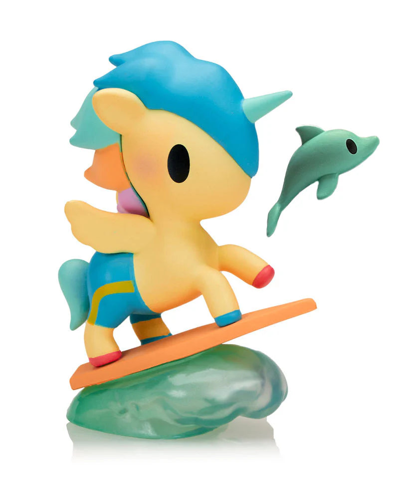 Fun In The Sun Unicorno Blind Box: Winged unicorn on surfboard riding a wave, with a tiny dolphin hovering nearby. A whimsical beach-themed collectible figure.