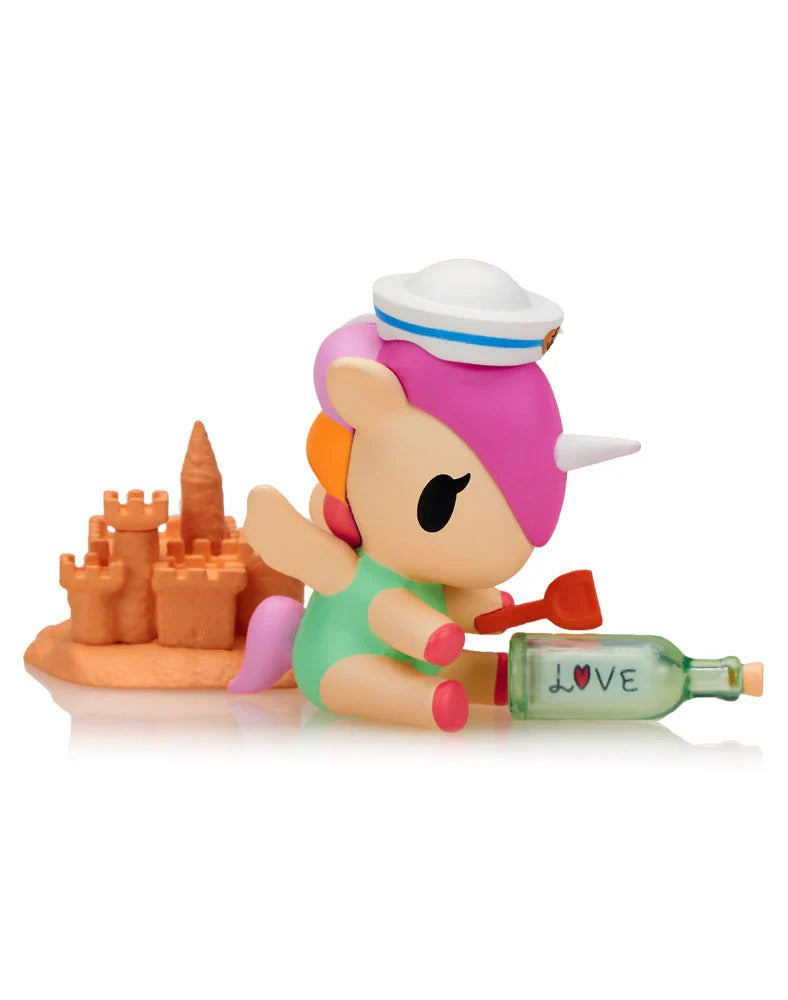Fun In The Sun Unicorno Blind Box featuring a pastel unicorn figurine in a sailor hat, building a sandcastle, with a tiny shovel and a LOVE bottle accessory.