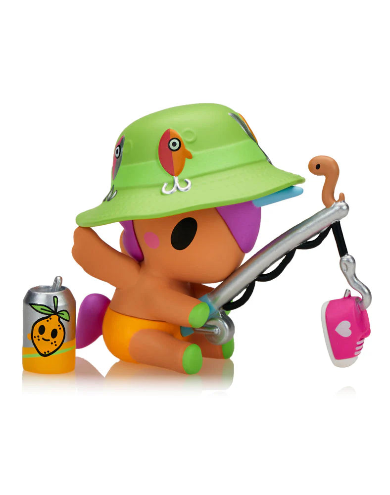 Fun In The Sun Unicorno Blind Box: A seated vinyl toy, orange body, purple hair, fishing gear, and colorful bucket hat, capturing a playful beach vibe.