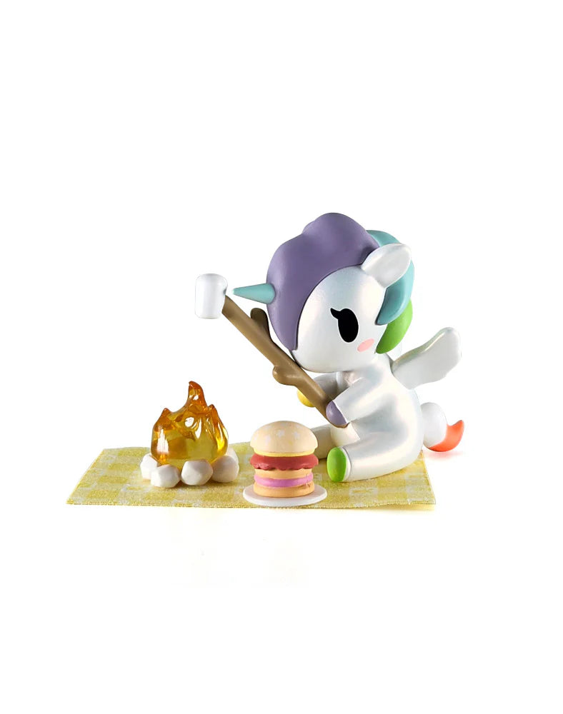 Picnic Party Unicorno Blind Box featuring a unicorn with camping accessories, including a marshmallow stick and mini sandwich on a checkered blanket.