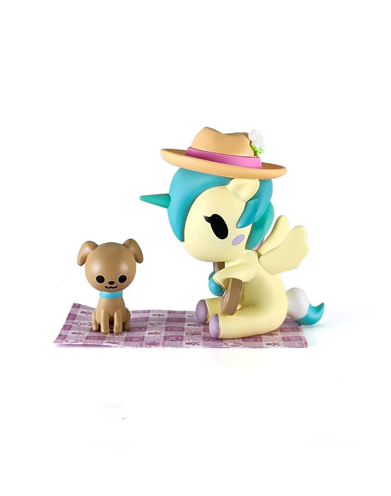 Picnic Party Unicorno Blind Box: Winged unicorn with a sunhat and book, and a puppy figurine on a gingham blanket, showcasing collectible art toys.