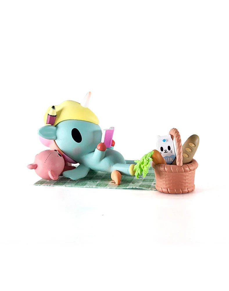 Picnic Party Unicorno Blind Box: Aqua unicorn figure lounging with accessories, including a picnic basket and handheld device, from tokidoki's collectible series.