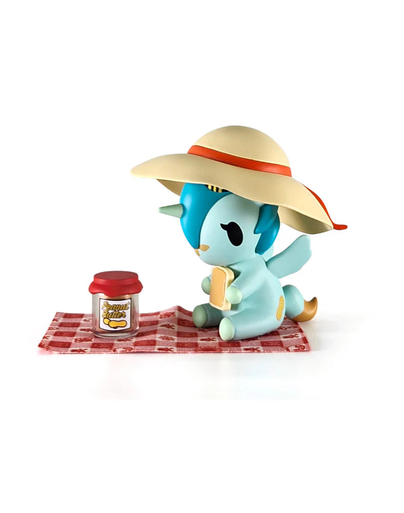 Picnic Party Unicorno Blind Box figure: pastel-blue unicorn with straw hat sits on a picnic cloth, holding bread, next to a peanut butter jar.