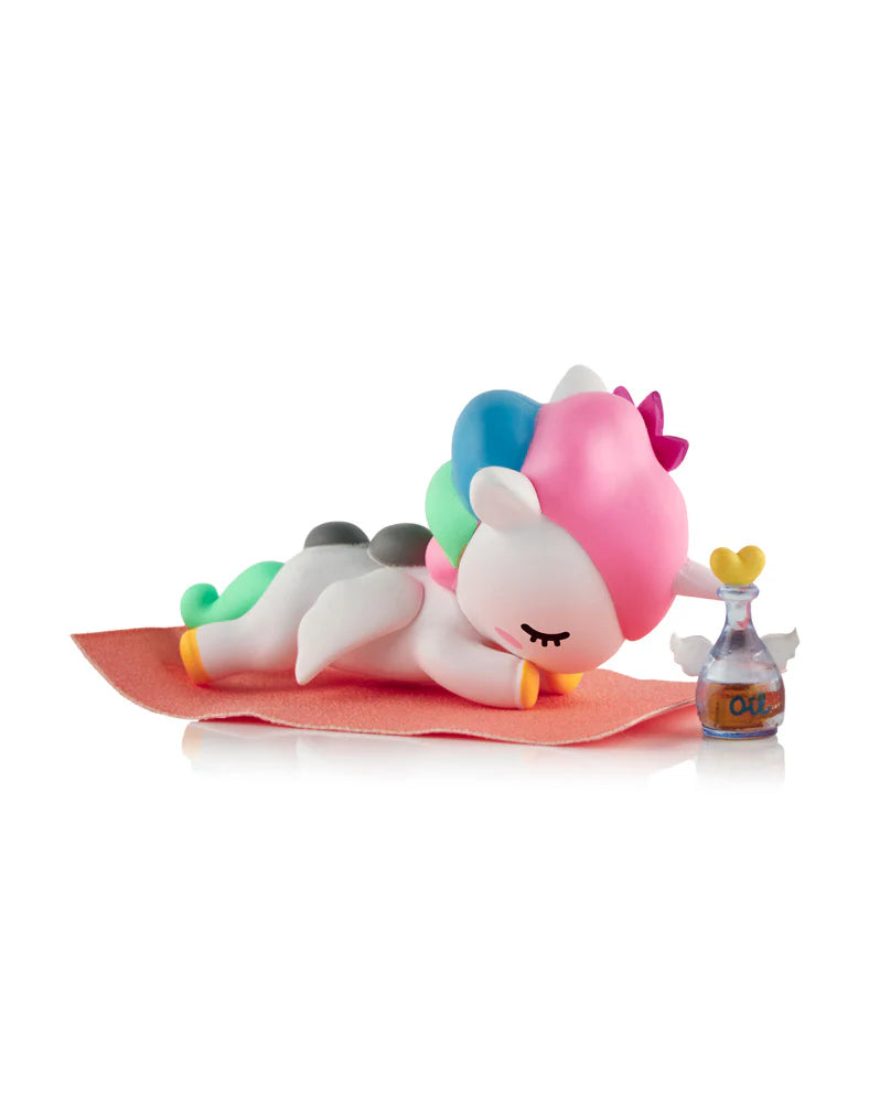 Spa Day Unicorno Blind Box - Preorder: A pastel unicorn figurine with mini wings, relaxing on an orange mat, paired with a heart-topped oil bottle.