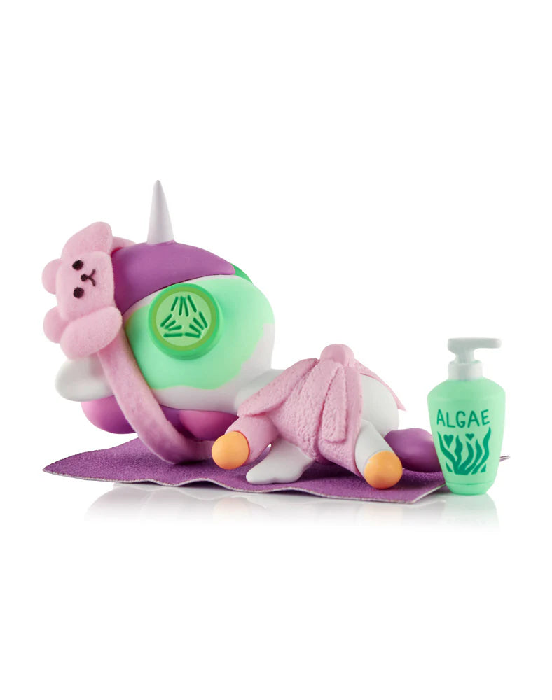 Spa Day Unicorno Blind Box - Preorder: Unicorn figurine on a mat, wearing a robe, headband, and facial mask, with an ALGAE bottle beside it.