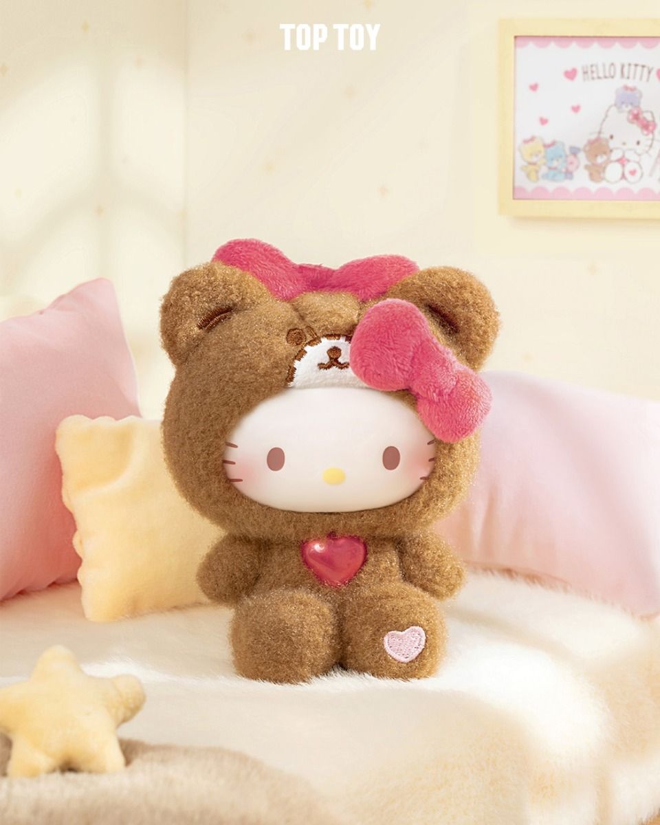 Plush Hello Kitty in brown bear costume from Sanrio Teddy Pajamas Plush Keychain Blind Box Series, on cream surface with pastel pillows, framed artwork behind. Preorder available.