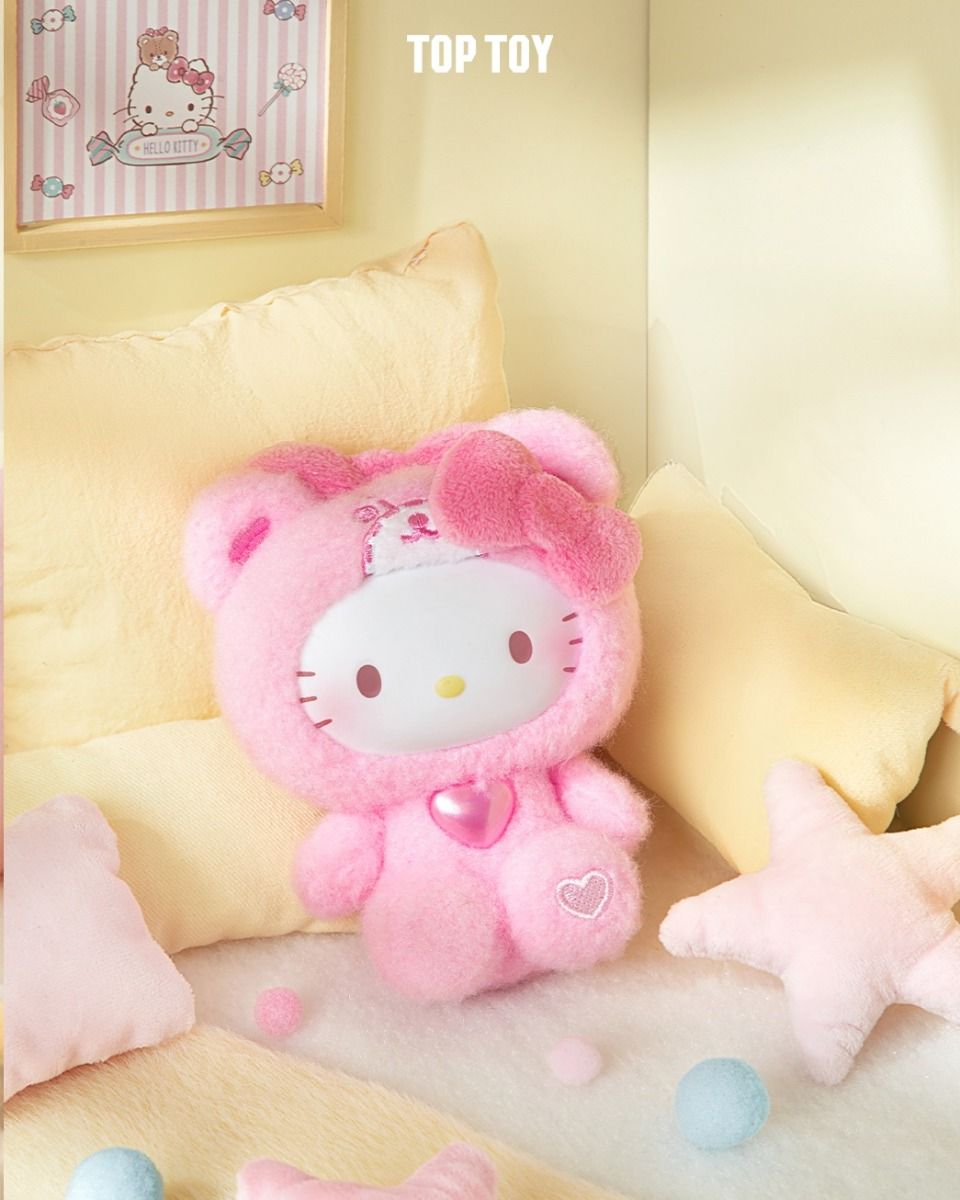 Hello Kitty in pink bear onesie, part of the Sanrio Teddy Pajamas Plush Keychain Blind Box Series - Preorder, surrounded by pillows and pom-poms.