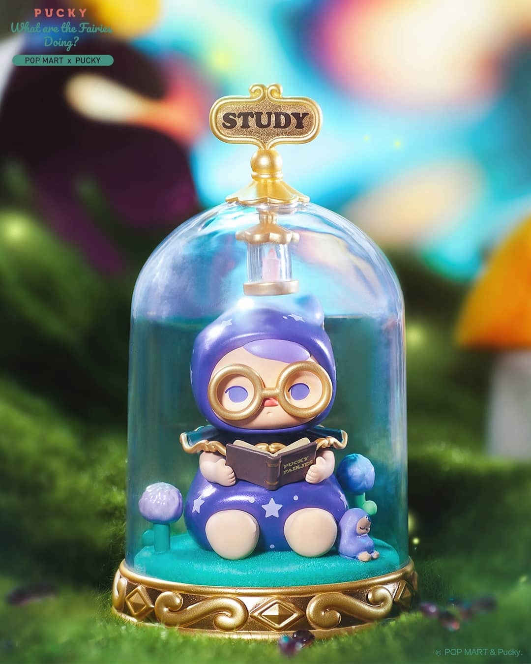 Pucky What Are The Fairies Doing Series toy figurine in a glass dome with a purple ball and a woman reading a book.