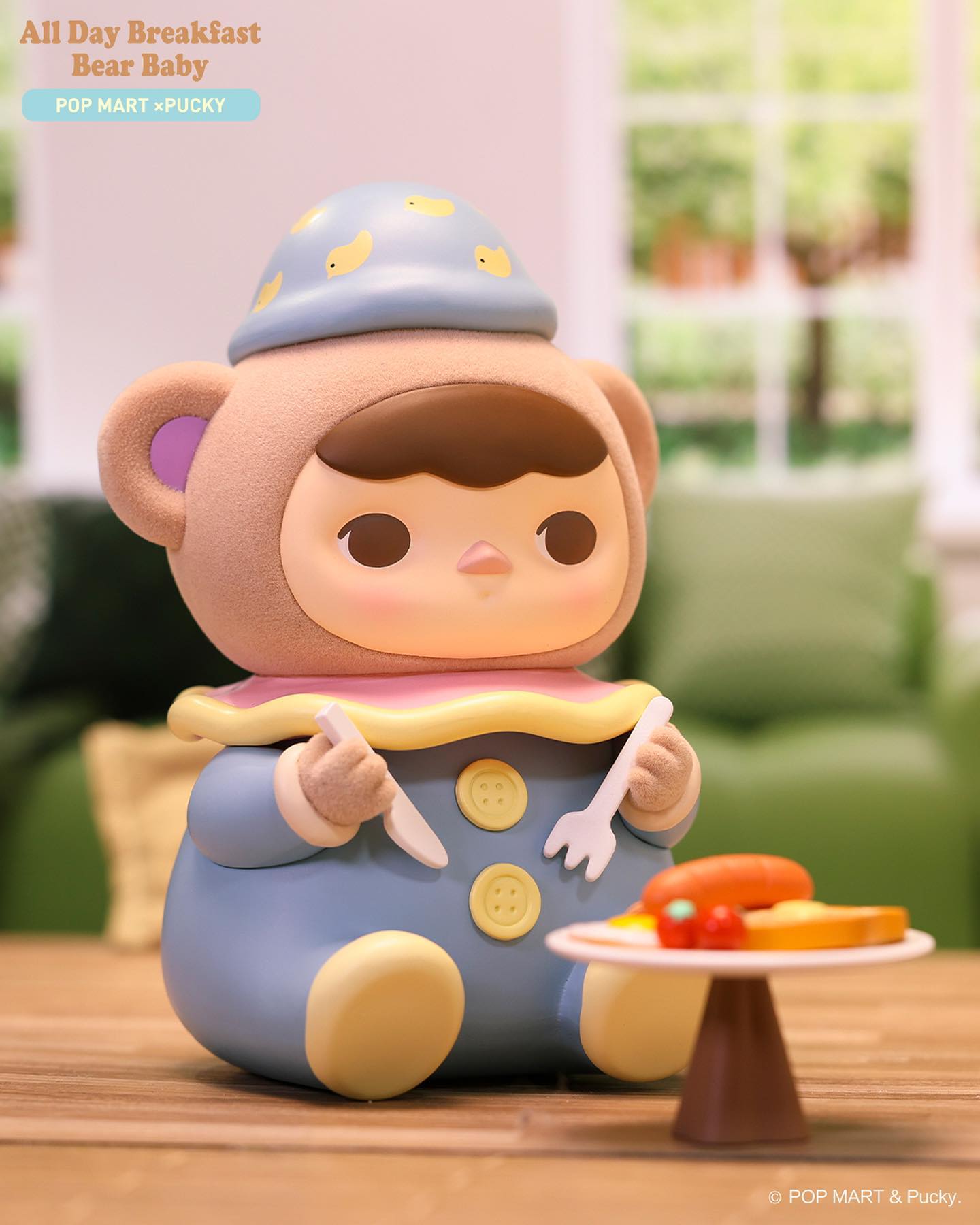 Toy figurine of All Day Breakfast Bear Baby by Pucky holding utensils, close-up of various baby toys.