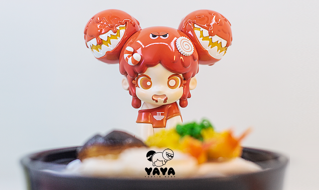 Yaya - Japanese Noodle figurine with orange hair and candy, a logo close-up, and orange objects on toy.