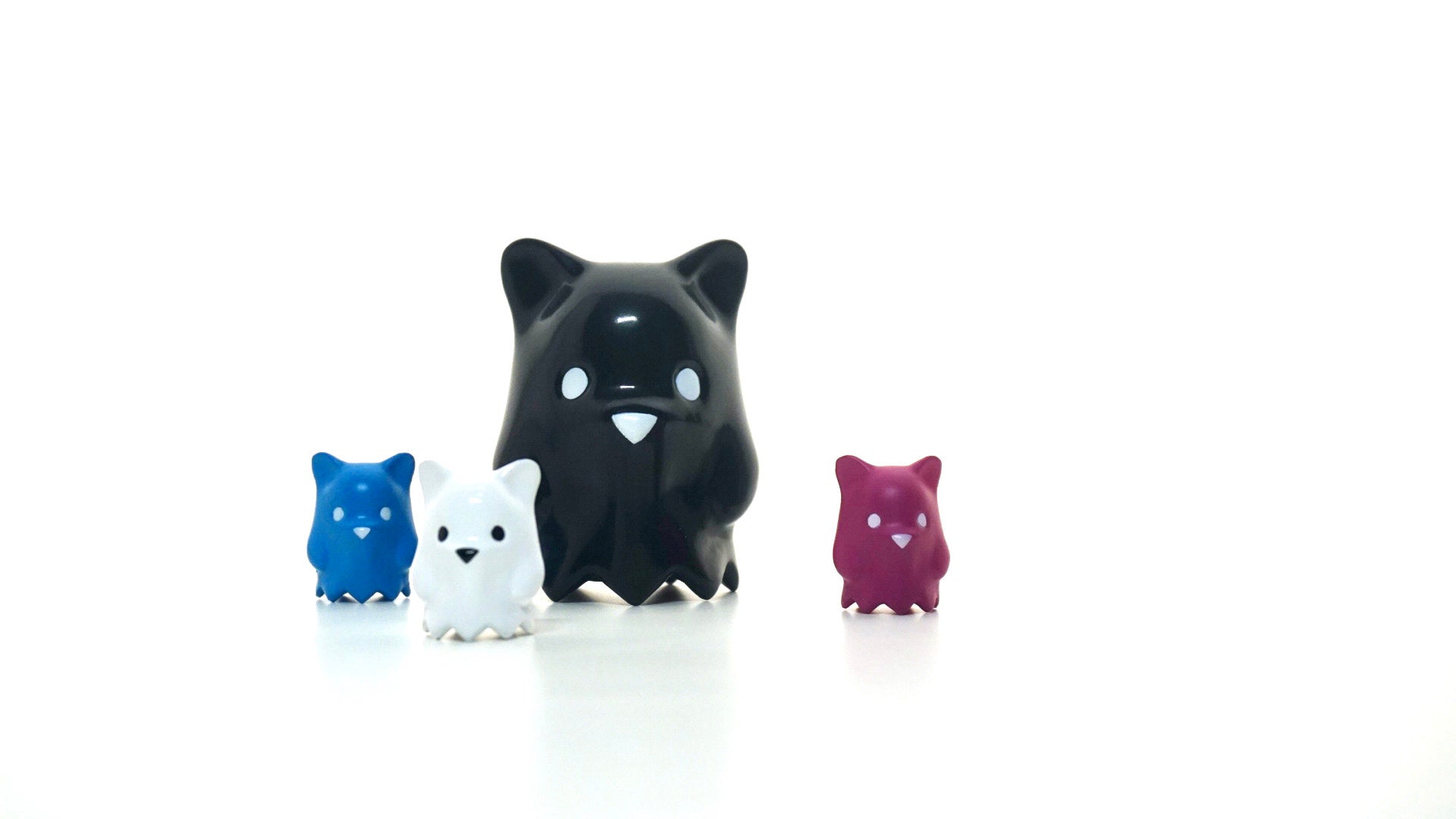 A group of small animal figures including a purple bear, white ceramic animal, black and white cat statue, and blue toy animal.
