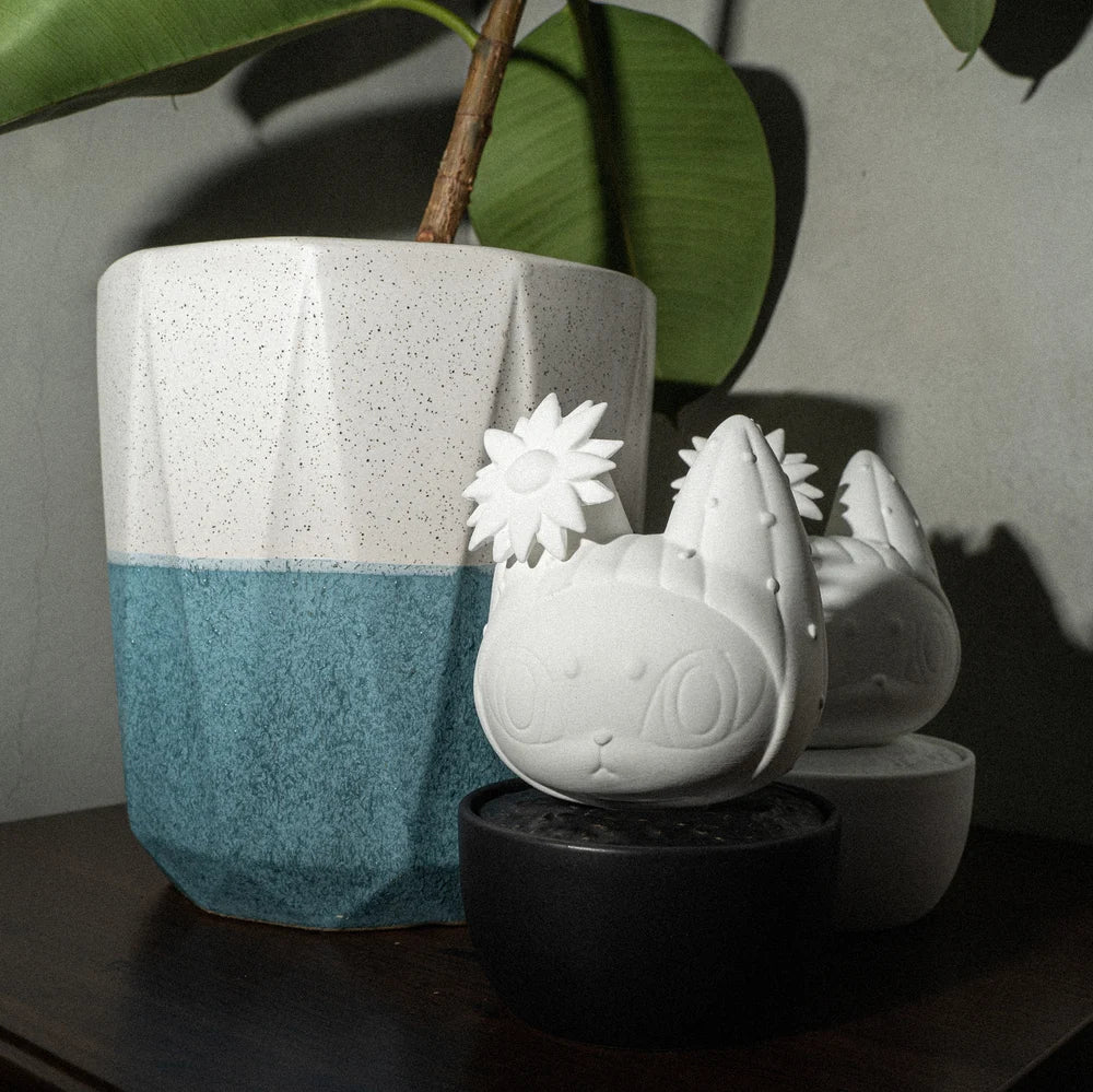 A houseplant in a pot next to a vase, a white cat statue, and a flower-shaped object.