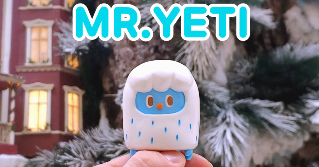 A hand holding Mr. Yeti toy with a blue face, close up of a person's finger, 6.5cm resin toy by 2oz.