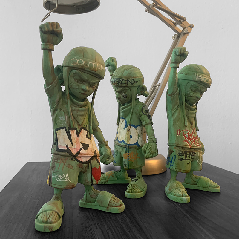 A group of green statues with graffiti, including a boy and a person, along with a toy and metal object, from the Enter The Fu - Skrew York 88 by Rios Palante collection.