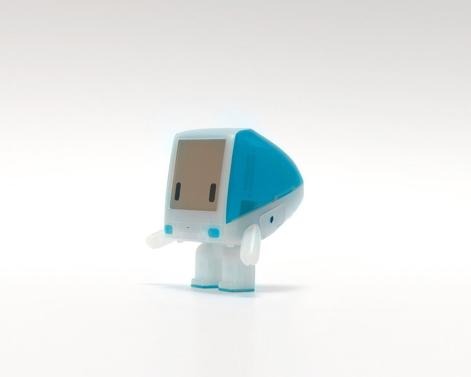 A small plastic toy resembling a classic computer with a screen and detachable arms, inspired by the iBot G3 by Philip Lee.