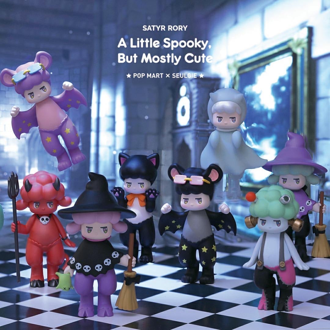 Satyr Rory A Little Spooky figurines on checkered surface, purple toy with stars, red toy with skull staff, bat figurine, animal with bow tie, person figurine, cartoon character with green hair, figure with white cape on chess board.